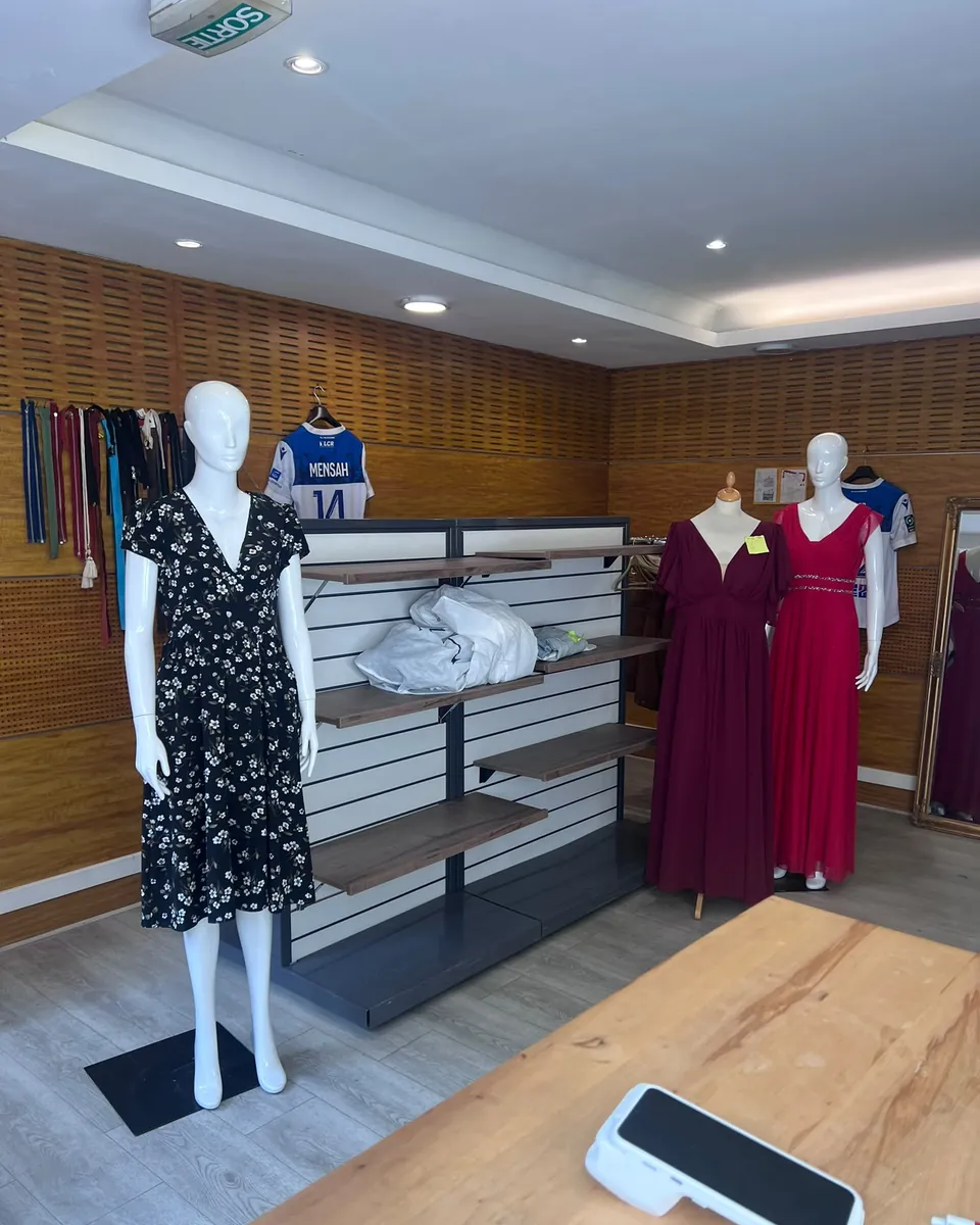 Intérieur de la boutique : robes de cérémonie et robe à fleurs sur des mannequins, grande table de travail en bois